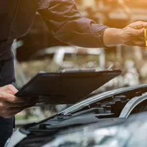 Mechanic inspecting car engine with clipboard