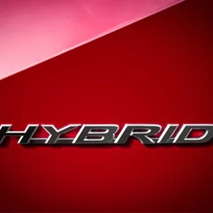 Close-up of chrome hybrid car badge on red background.